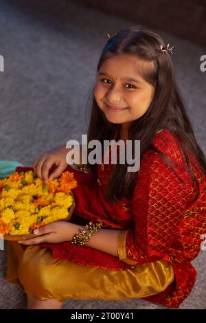 Fille joyeuse assise avec une assiette de fleurs à l'occasion de Diwali Banque D'Images