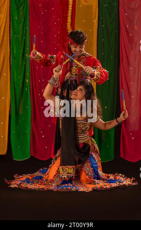 Couple indien habillé en tenue culturelle faisant de la danse folklorique garba avec des bâtons de dandia pendant les célébrations Navratri Banque D'Images