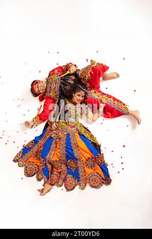 Heureux couple de Gujarati vêtus d'une tenue traditionnelle Gujrati, pose pour une photographie alors qu'ils sont allongés sur le sol tenant des bâtons de dandia, pendant Navratri ce Banque D'Images