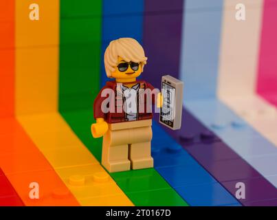 Tambov, Fédération de Russie - 01 octobre 2023 Une minifigurine Lego utilisant un smartphone et debout sur un fond arc-en-ciel. Banque D'Images