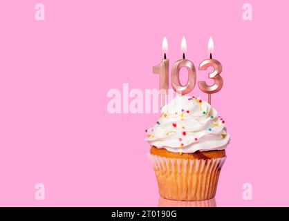 Gâteau d'anniversaire avec bougie numéro 103 - sur fond rose. Banque D'Images