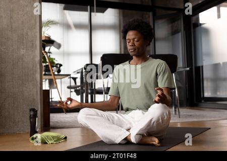 Heureux homme afro-américain détendu pratiquant la méditation de yoga assis sur le sol à la maison Banque D'Images