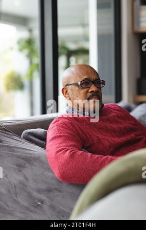 Homme biracial senior réfléchi portant des lunettes assis sur le canapé à la maison Banque D'Images