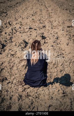 Femme réfléchie et triste assise sur le sol dans un champ sec en raison du changement climatique Banque D'Images