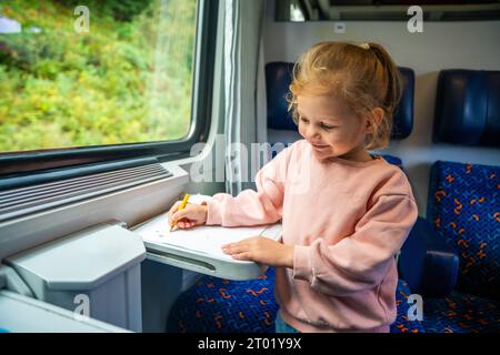 Belle petite fille dessine avec des crayons sur du papier blanc tout en voyageant en train en Europe Banque D'Images