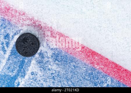 Regardant vers le bas sur un palet de hockey sur glace noir labourant à travers la neige et s'arrêtant sur le bord de la ligne de but du pli de but. Banque D'Images