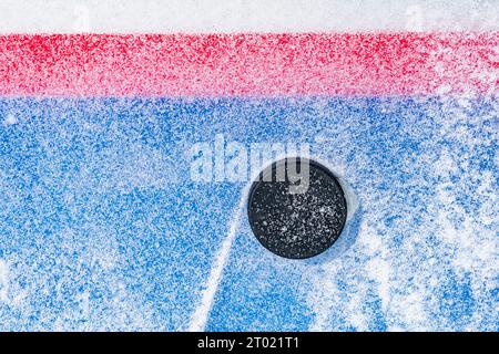 Regardant vers le bas sur un palet de hockey sur glace noir labourant à travers la neige et s'arrêtant sur le bord de la ligne de but du pli de but. Banque D'Images