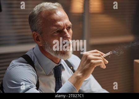 Portrait ambiant de beau détective senior étudiant le cas dans le bureau et le tabagisme Banque D'Images