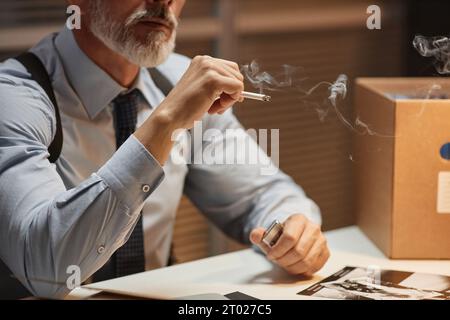 Gros plan d'un détective masculin mature fumant la cigarette dans le bureau de police, espace de copie Banque D'Images