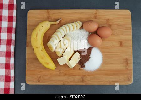vue d'en haut sur les ingrédients pour un gâteau, banane, oeufs, farine, sucre et beurre sur une planche Banque D'Images