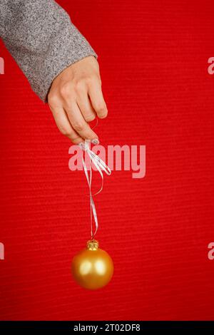 Boule ronde rouge d'arbre de Noël dans la main femelle isolé sur fond rouge. Une main de femme tient un jouet décoratif d'arbre de Noël. Nouvel an et Noël Banque D'Images