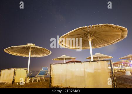 Chaises longues sous parasols sur fond de ciel nocturne et voie lactée Banque D'Images