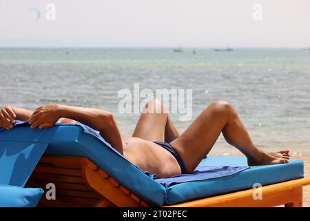 Vacances à la plage, homme bronzant dans une chaise longue sur la côte de la mer Banque D'Images