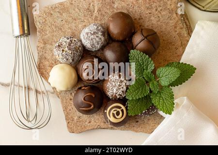 truffes au chocolat sur une pierre avec des feuilles de menthe et un fouet Banque D'Images