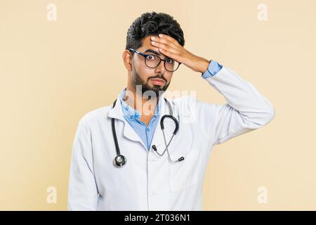 Paume du visage. Honte à toi. Bouleversé triste jeune médecin indien cardiologue homme faisant le geste de la paume du visage, se sentant ennuyé, , déçu dans le résultat, mauvaise nouvelle. Homme de pharmacie apothicaire arabe sur fond beige Banque D'Images