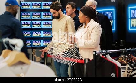 Les femmes obsédées se battent pour le panier, devenant folles sur les ventes saisonnières du vendredi noir dans le centre commercial. Clients agressifs anxieux entrant dans le magasin de vêtements, agent de contrôle des foules. Prise de vue à main levée. Banque D'Images