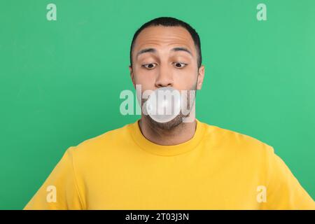 Portrait de jeune homme soufflant de la gomme à bulles sur fond vert Banque D'Images