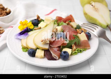 Salade savoureuse avec fromage brie, prosciutto, noix et poire sur table carrelée blanche, closeup Banque D'Images