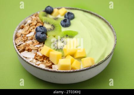 Savoureux bol de smoothie matcha servi avec des fruits frais et des flocons d'avoine sur fond vert, gros plan. Petit déjeuner sain Banque D'Images