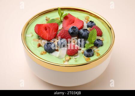 Savoureux bol de smoothie matcha servi avec des baies et des flocons d'avoine sur fond beige, gros plan. Petit déjeuner sain Banque D'Images