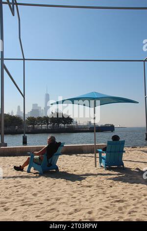 New York, États-Unis. 03 octobre 2023. Les amateurs de plage prennent le soleil sur la première plage de Manhattan, la « péninsule de Gansevoort ». A la fin de l'été, de tous les temps, Manhattan a sa première plage. Avec du sable, des parasols, des chaises longues et une vue sur la Statue de la liberté et le nouveau World Trade Center, le nouveau crédit : Christina Horsten/dpa/Alamy Live News Banque D'Images