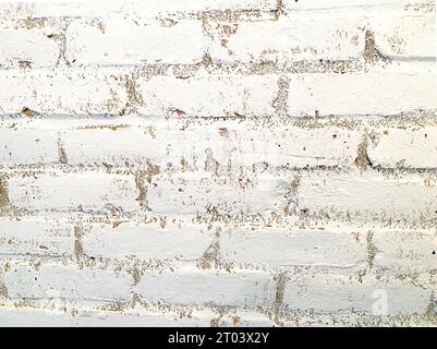 Mur de briques blanches en gros plan. Mur intérieur en briques, peint en blanc avec un peu de saleté et imparfaite, texture rugueuse, usée par le temps. Convient comme arrière-plan. Banque D'Images