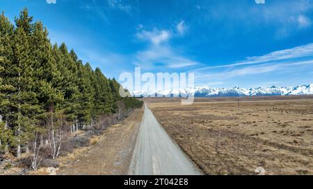 Longue route de gravier sinueuse et étroite à travers la campagne agricole rurale vers la chaîne de montagnes enneigée des alpes du Sud Banque D'Images