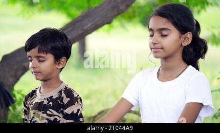 Portrait de magnifique enfant pratiquant le yoga en plein air. Bel enfant pratique le yoga asana ou fait des exercices de gymnastique. Petits enfants méditant dans lotus po Banque D'Images