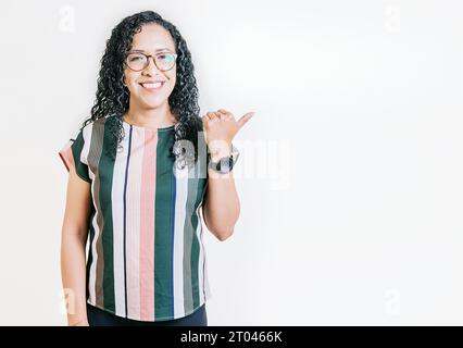 Souriant des latins pointant une bannière sur le côté. Heureuse femme latine recommandant avec les doigts isolés. Joyeuse fille aux cheveux bouclés pointant un Banque D'Images
