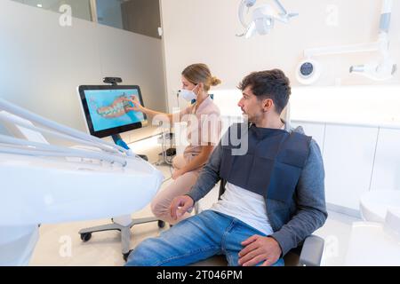 Dentiste utilisant la technologie moderne pour expliquer la procédure dentaire à un homme assis sur la clinique Banque D'Images