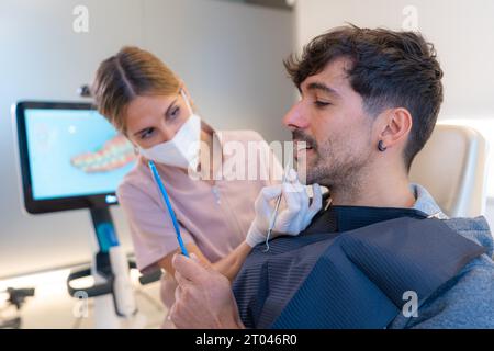 Dentiste portant un masque chirurgical à l'aide d'un miroir pour montrer les résultats à un patient Banque D'Images