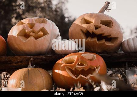 Tête de citrouille d'Halloween avec visage souriant sculpté et effrayant sur banc de bois à l'extérieur. Jack-O-Lantern, bougies allumées, feuilles séchées à l'extérieur. Halloween Composi Banque D'Images