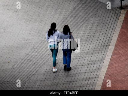 Vue arrière de deux jeunes femmes marchant ensemble sur le trottoir d'une rue par temps gris. Banque D'Images