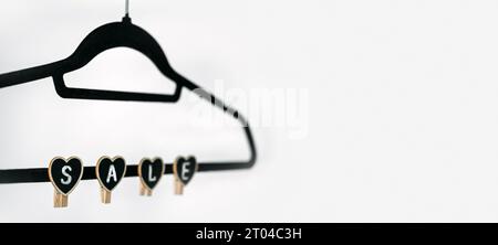 Concept de vente Black Friday avec vêtements noirs Hanger et signe de forme de coeur VENTE sur blanc. Magasin, concept d'achat, vente, conception, cintre vide. Banque D'Images