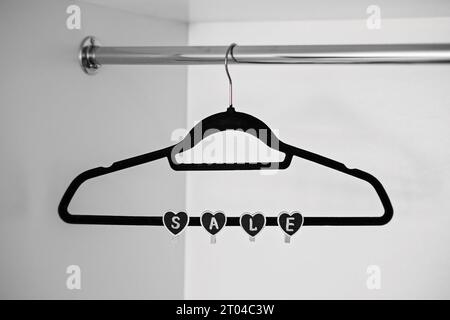 Concept de vente Black Friday avec vêtements noirs Hanger et signe de forme de coeur VENTE sur blanc. Magasin, concept d'achat, vente, conception, cintre vide. Banque D'Images