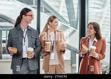 trois collègues ayant la pause déjeuner souriant sincèrement et mangeant des sandwichs, concept de coworking Banque D'Images