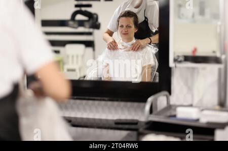 La coiffeuse met un sac en papier autour du cou de la femme pour protéger les vêtements qu'elle coupe les cheveux à l'intérieur Banque D'Images