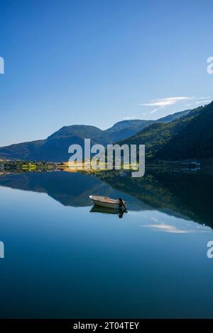 Un bateau à moteur flotte dans les eaux calmes de Barsnesfjorden près de Krossen, en Norvège, au cours d'une matinée sans nuages où les montagnes environnantes se reflètent Banque D'Images