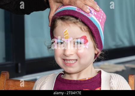 Dans un moment fantaisiste de pur délice, une petite fille se transforme en licorne magique avec son visage peint Banque D'Images