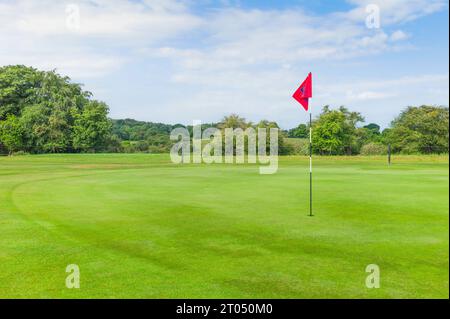 Vert du golfeur avec poteau et drapeau rouge et vue sur le parc public Westwood sous le ciel bleu et les nuages par un beau matin de printemps à Beverley, Royaume-Uni. Banque D'Images