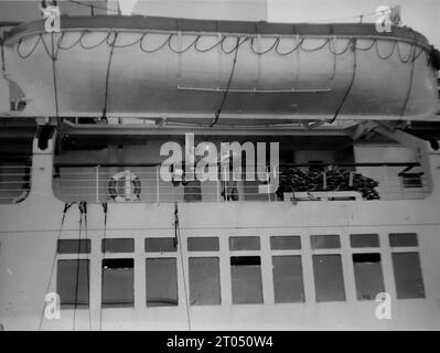 Vue rapprochée depuis le quai d’une partie du R.M.S. Queen Mary, avec des gens debout sous l’un des canots de sauvetage du navire. Cette photographie est tirée d'un album personnel non attribué de photographies d'une croisière à New York datée du 29 juin au 13 août 1956. Départ de Liverpool à bord du navire Cunard M.V. Britannic et retour de New York à Southampton à bord du navire Cunard R.M.S. Queen Mary. La taille moyenne des photographies originales était de 4x3 pouces. Banque D'Images