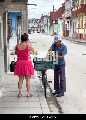 Un cubain âgé et mince vend des aliments dans un vieux vélo. Une femme lui achète. La scène se passe dans une rue de la ville.Santa Clara, Cuba, 2023 Banque D'Images