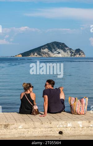 jeune couple assis sur la digue de la mer à la plage sur l'île grecque de zante ou zakynthos regardant vers la mer à l'île de marothonisi au large de la côte de keri Banque D'Images