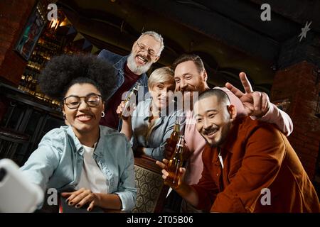 heureuse femme afro-américaine prenant selfie sur smartphone avec des amis multiethniques avec des bouteilles de bière Banque D'Images