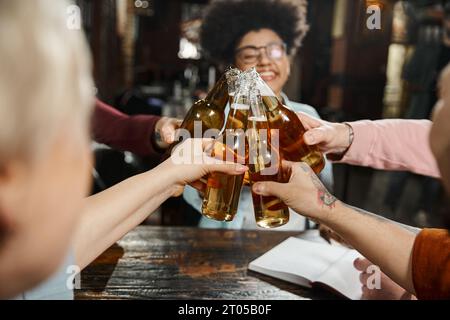 les gens d'affaires multiculturels se détendent dans le pub après le travail et clinking bouteilles de bière, happy time Banque D'Images