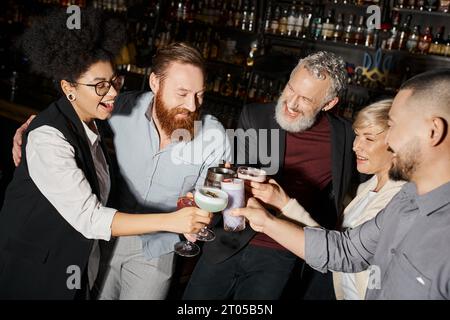 les hommes barbus et les femmes heureuses clinquant des lunettes dans le bar, après les loisirs de travail de collègues multiethniques Banque D'Images