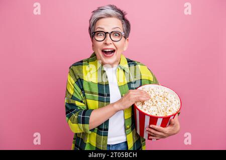 Portrait de la personne extatique overjoyed avec des cheveux gris habillés chemise à carreaux élégant tenir le pop-corn regardant le film isolé sur fond de couleur rose Banque D'Images