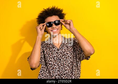 Portrait de belle personne drôle avec chevelure Wear chemise de léopard mains touchant lunettes de soleil souriant isolé sur fond de couleur jaune Banque D'Images