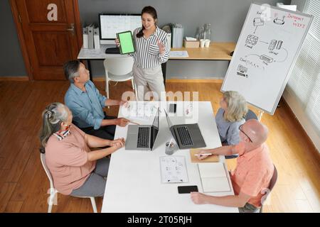 Jeune femme montrant l'ordinateur tablette avec écran vert aux aînés dans la classe d'informatique Banque D'Images