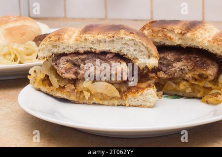 Un gros plan de deux moitiés d'un hamburger avec du pain grillé sur une assiette en céramique, placé sur un comptoir rustique, avec des oignons dorés en arrière-plan et un Banque D'Images